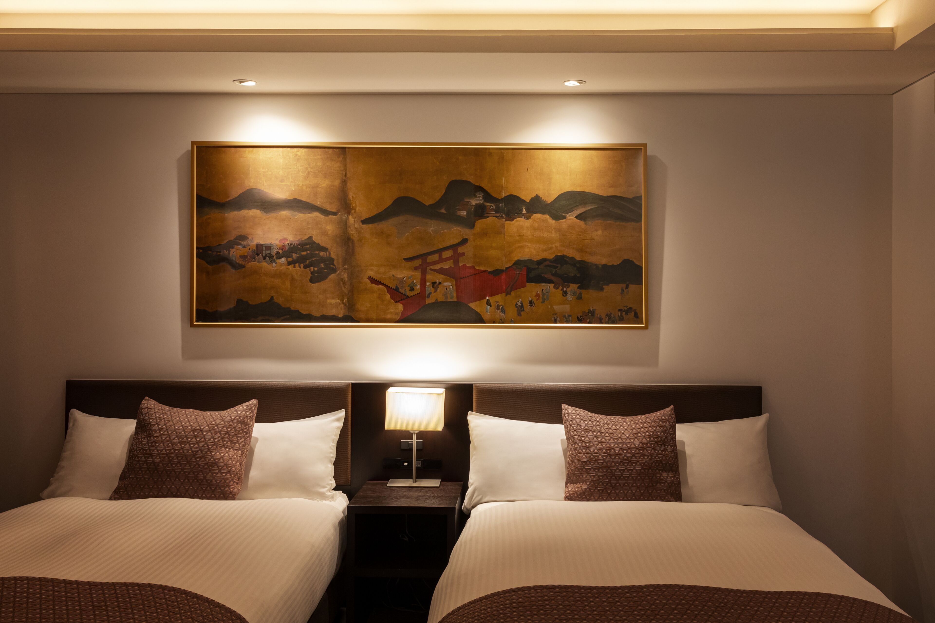 A hotel room with two beds, a nightstand, a lamp, and a large painting on the wall.