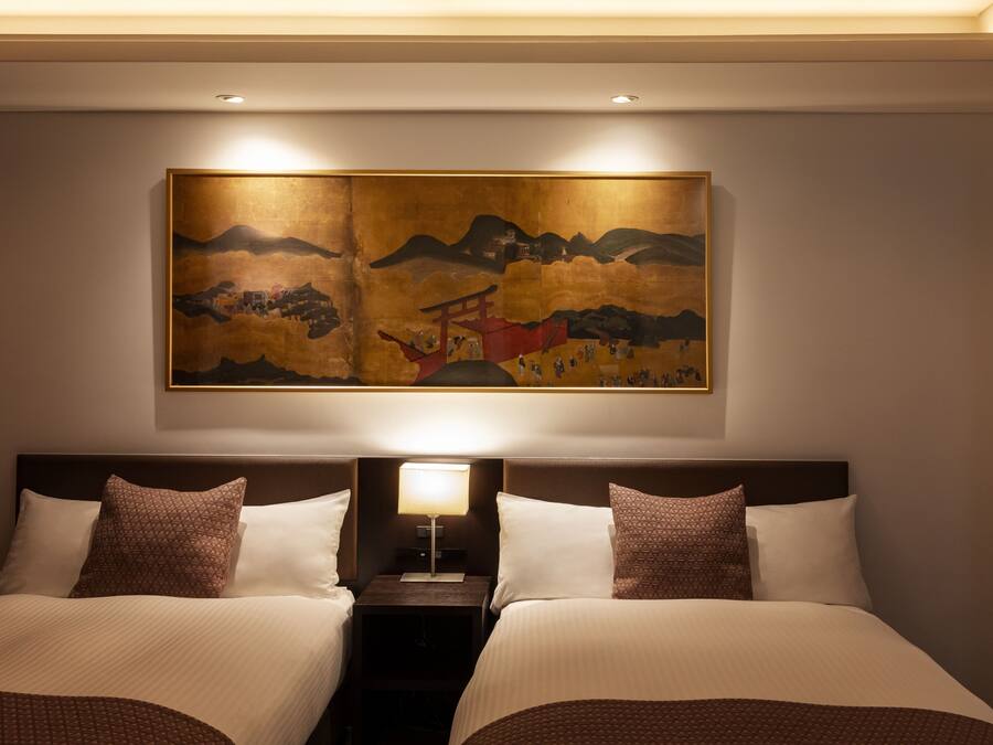 A hotel room with two beds, a nightstand, a lamp, and a large painting on the wall.