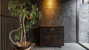 A modern interior with a bonsai tree in a woven pot, a wooden chest with intricate carvings, and a textured wall with a light fixture. - Rinn Gion Hanatouro (Kyoto)