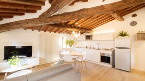 A modern kitchen with white cabinets, a refrigerator, and a microwave. There is a dining table with chairs and a TV in the living area. - Sibilla Luxury Flat in center town (Lucca)