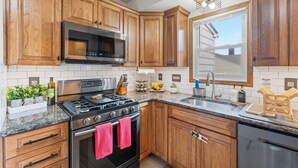 Una cocina con armarios de madera, electrodomésticos de acero inoxidable, encimera de granito y ventana con vistas al exterior.