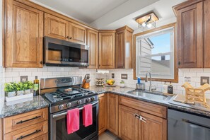 Cucina con mobili in legno, elettrodomestici in acciaio inossidabile, piano di lavoro in granito e finestra con vista all'esterno.