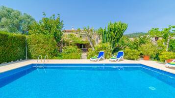 A swimming pool with two lounge chairs, surrounded by greenery and a building in the background.