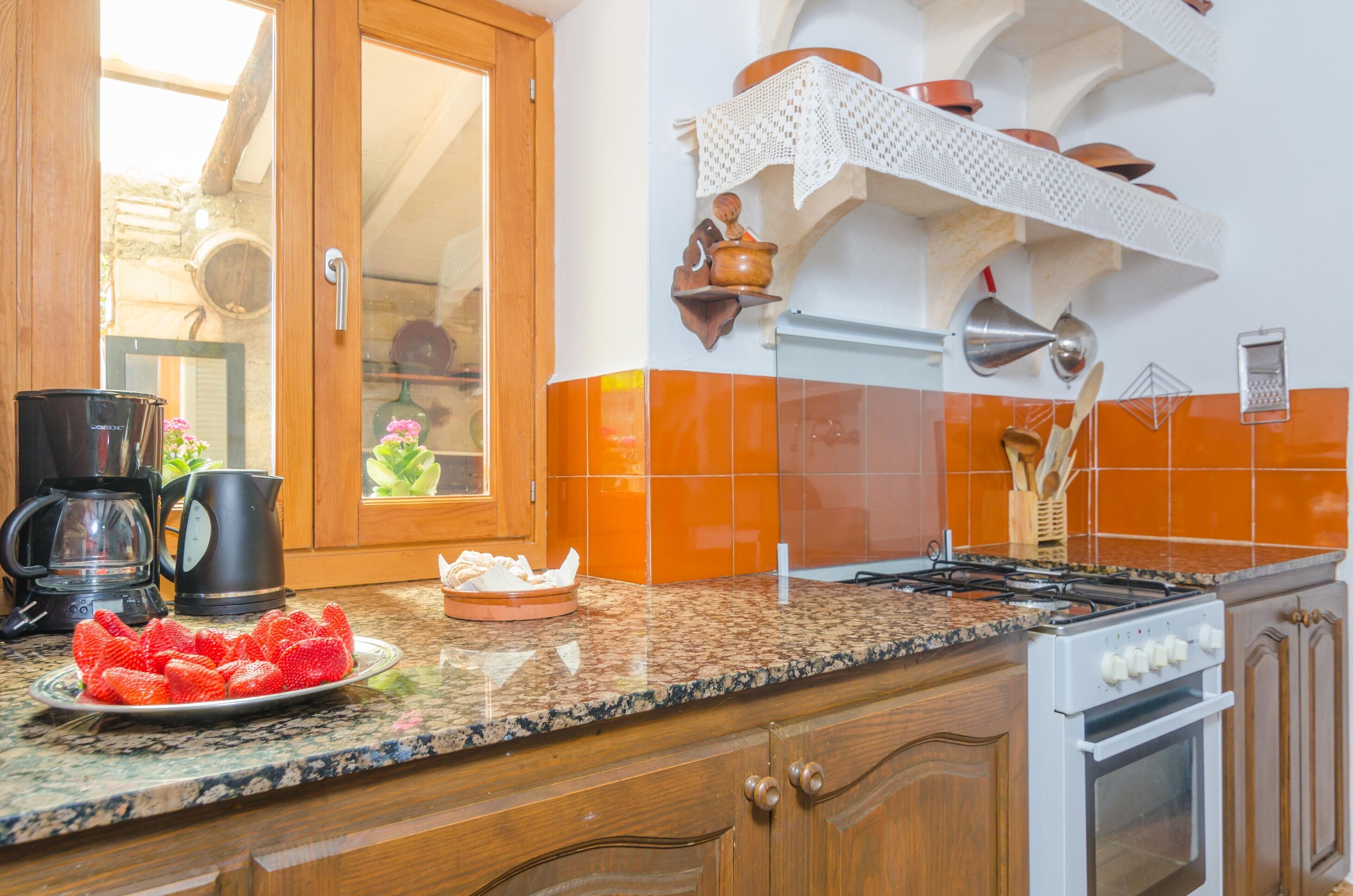 A kitchen with a granite countertop, wooden cabinets, a stove, and a coffee maker.