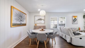 Un salon moderne avec une table de salle à manger ronde, des chaises à revêtement gris, un canapé blanc et un lustre.