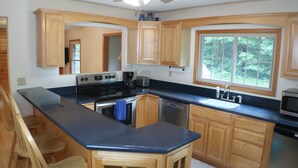 A kitchen with wooden cabinets, a black countertop, a stove, a sink, and a window with a view of trees. - Cozy Countryside Stone House & Pub with 20 acres of outdoor fun! (Morley)