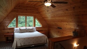 A bedroom with a bed, a nightstand, a desk, a ceiling fan, and a window with a view of trees. - Cozy Countryside Stone House & Pub with 20 acres of outdoor fun! (Morley)