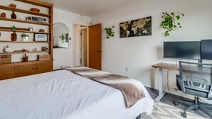 A bedroom with a bed, a desk with a chair, a television, and shelves with various items.