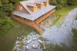 Une maison flottante en bois, dotée d’une terrasse, d’un escalier et d’une petite structure circulaire au niveau du sol.