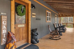 A cabin with a wooden door, a welcome sign, a number sign, a coat rack, and a bear sculpture.