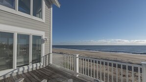 Eine Holzterrasse mit weißen Geländern, die auf einen Strand blickt.