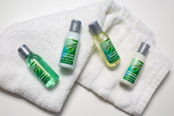 Cuatro botellas de productos para el cuidado corporal Rainkiss Leaves sobre una toalla blanca.