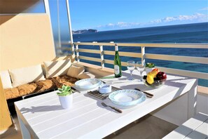 Enjoy a meal with a view of the ocean from this balcony dining area, featuring a table set with plates, a bottle, fruit, and cutlery.