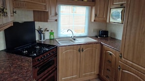 A kitchen with wooden cabinets, a stove, a sink, and a window with blinds.