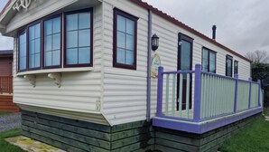 A mobile home with a porch, large windows, and a small deck.
