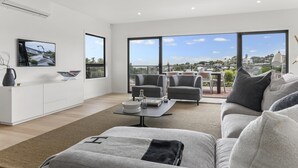 A modern living room with a large window, a flat-screen TV, and a sofa. - Luxury Mission Bay Oasis with Heated Pool (Auckland)