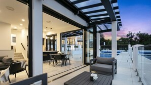 A modern outdoor living area with a pool, a dining area, and a covered patio. - Luxury Mission Bay Oasis with Heated Pool (Auckland)
