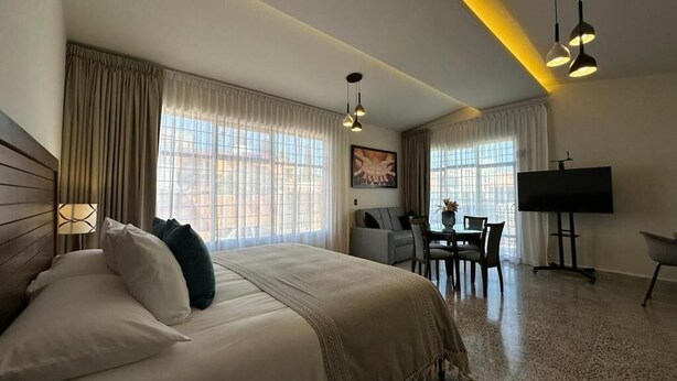 A hotel room with a large bed, a desk with a chair, a television, and a window with curtains. - Casa Sofía (Atlacomulco)