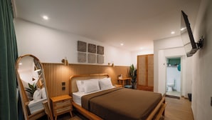 A modern bedroom with a wooden bed, bedside tables, a mirror, and a TV mounted on the wall. - Snooze Hostel Malang (Malang)