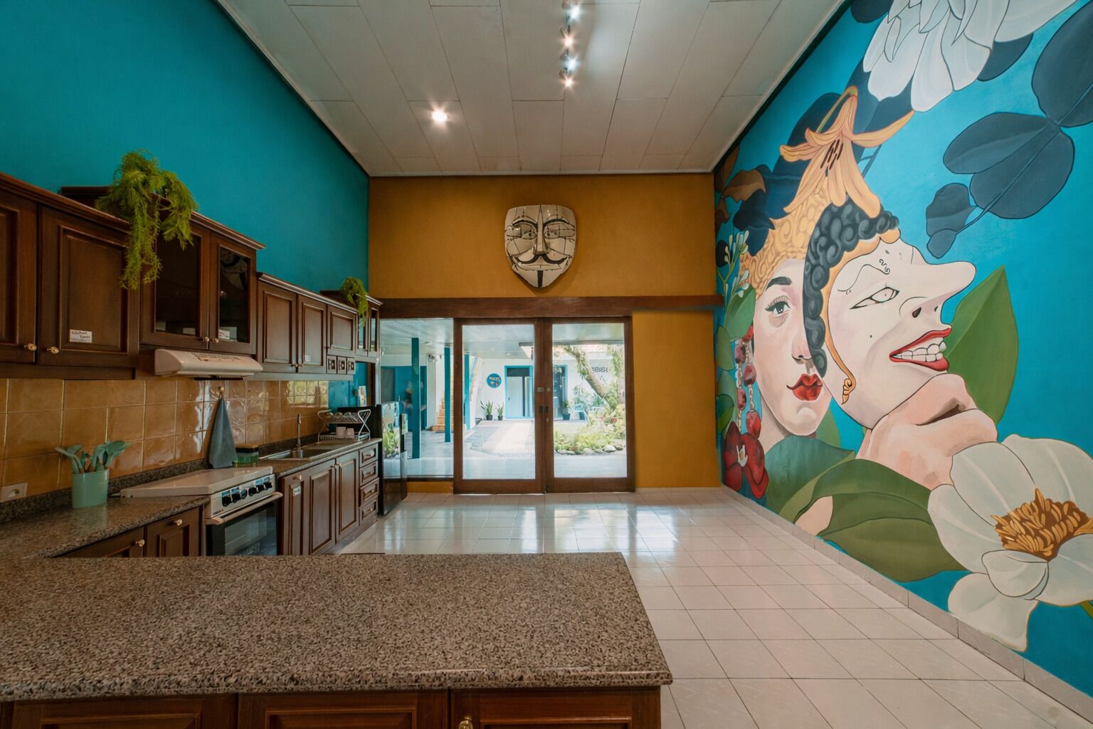 A kitchen with granite countertops, wooden cabinets, and a mural of a woman on the wall.