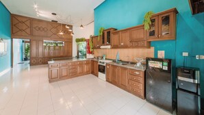 A spacious kitchen with wooden cabinets, a large island, and modern appliances including a refrigerator and oven. - Snooze Hostel Malang (Malang)