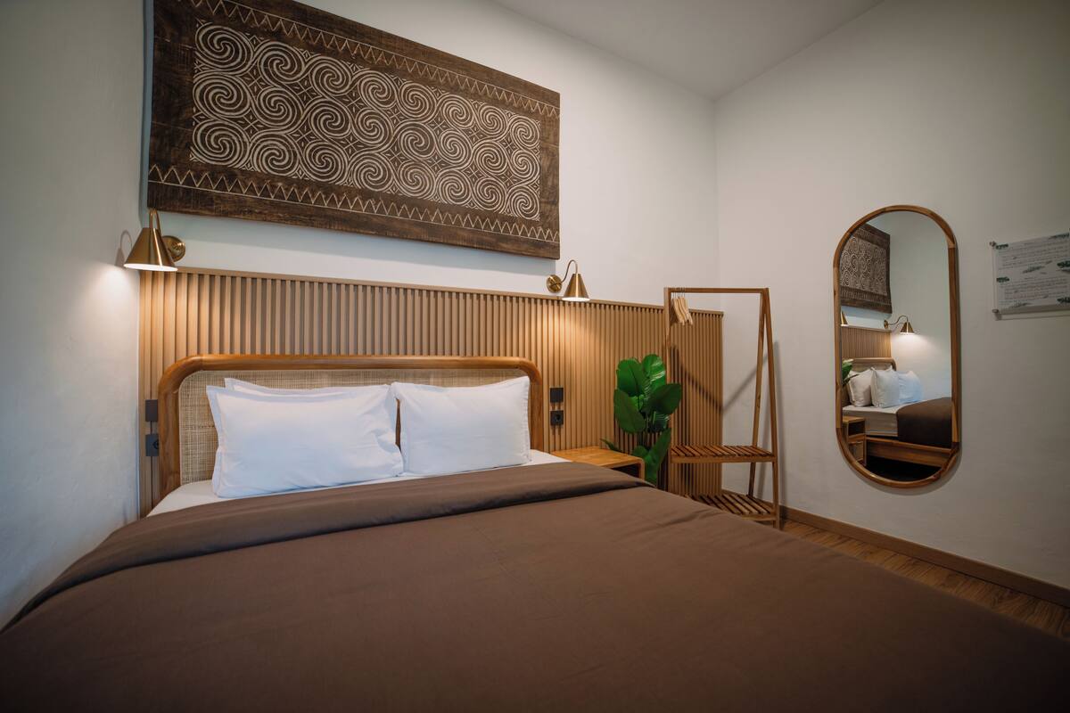 A neatly made bed with a wooden headboard, a wall-mounted mirror, and a decorative panel above the bed.