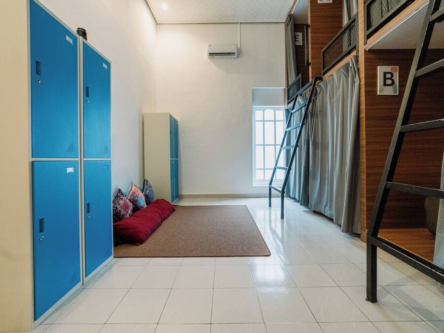 Habitación de hotel con taquillas azules, un sofá rojo, un tapete marrón y una escalera de madera.