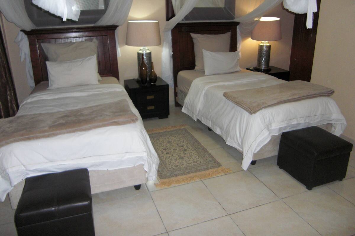Una habitación de hotel con dos camas, una mesita de noche y un pequeño otoman.