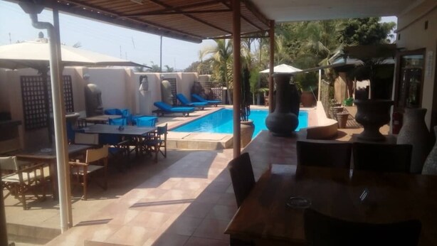A poolside area with a covered patio, lounge chairs, and a dining table. - Shamba Lodge (Kitwe)