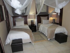 A hotel room with two beds, a nightstand, a lamp, and a small ottoman.