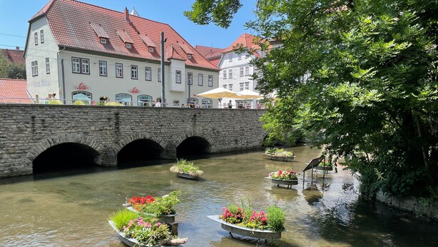 A stone bridge over a river with flower-filled boats, a building with a red-tiled roof, and a tree-lined path. - Apartment 'Ferienwohnung Beyer Friedrichroda' with Private Terrace, Private Garden and Wi-Fi (Friedrichroda)