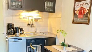 A compact kitchenette with a coffee maker, kettle, and microwave. There is a small dining table with a chair and a potted plant. - Apartment 'Ferienwohnung Beyer Friedrichroda' with Private Terrace, Private Garden and Wi-Fi (Friedrichroda)