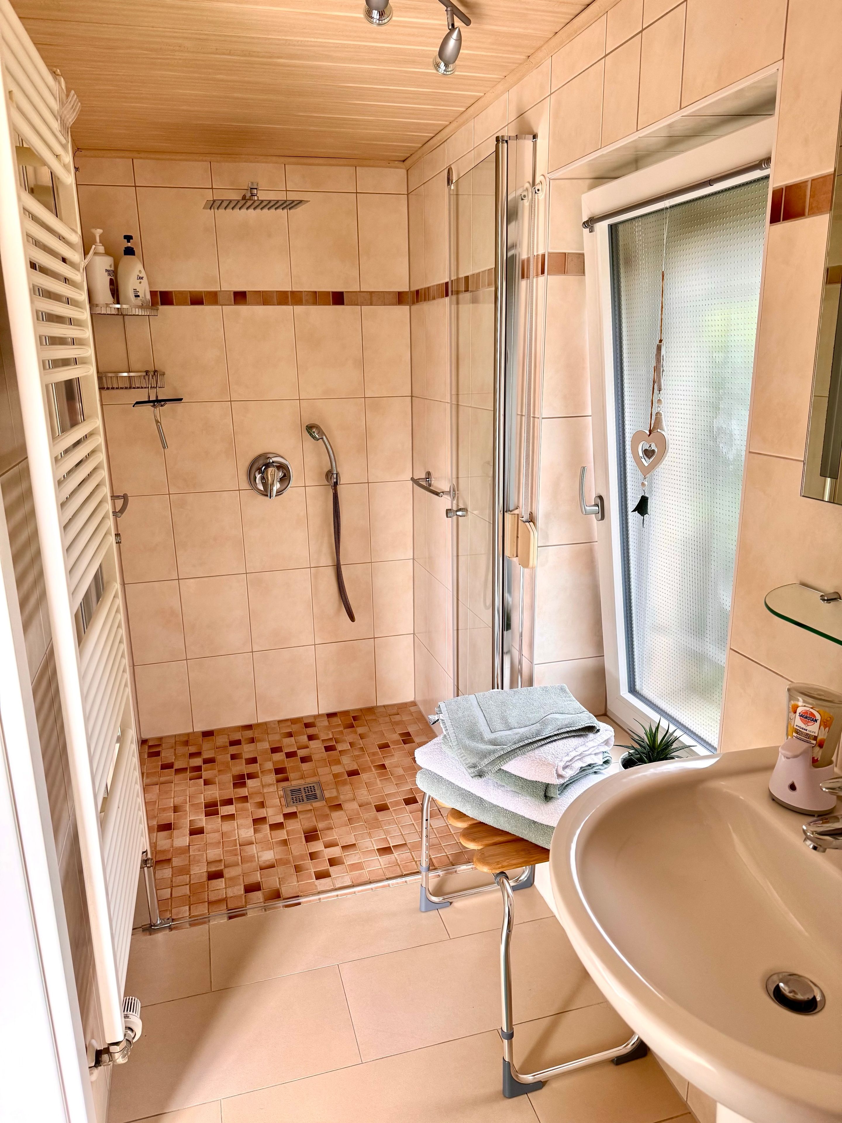 Ein Badezimmer mit Dusche, Waschbecken und Fenster.