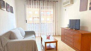 Een woonkamer met een bank, een houten tafel, een tv op een houten kast en een raam met gordijnen.