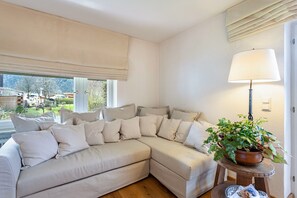 A beige sectional sofa with multiple cushions, a potted plant on a wooden stool, and a lamp on a side table.