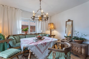 A traditional room with a wooden bench, a table with a white tablecloth, a chandelier, and a mirror on the wall.
