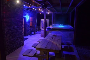 Uma área de estar ao ar livre com mesa e bancos de madeira, uma banheira de hidromassagem e uma parede de pedra.