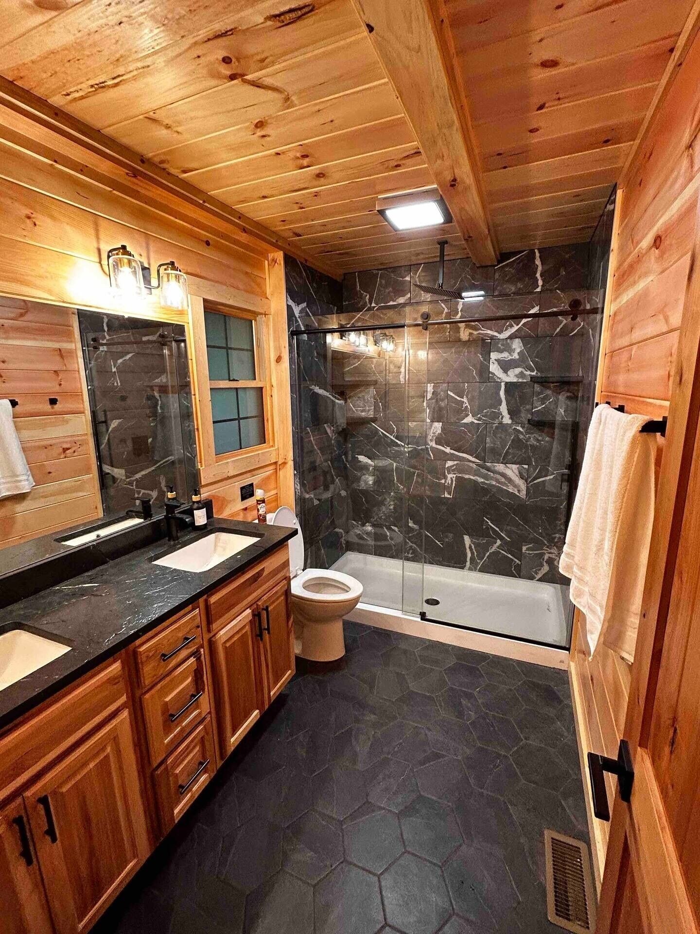 A wooden cabin bathroom with a marble shower wall, a bathtub, and a vanity with a sink and mirror.
