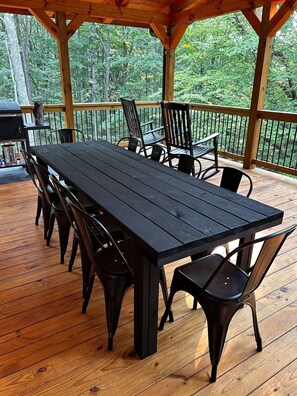 A wooden deck with a black table and chairs, surrounded by a railing and trees.