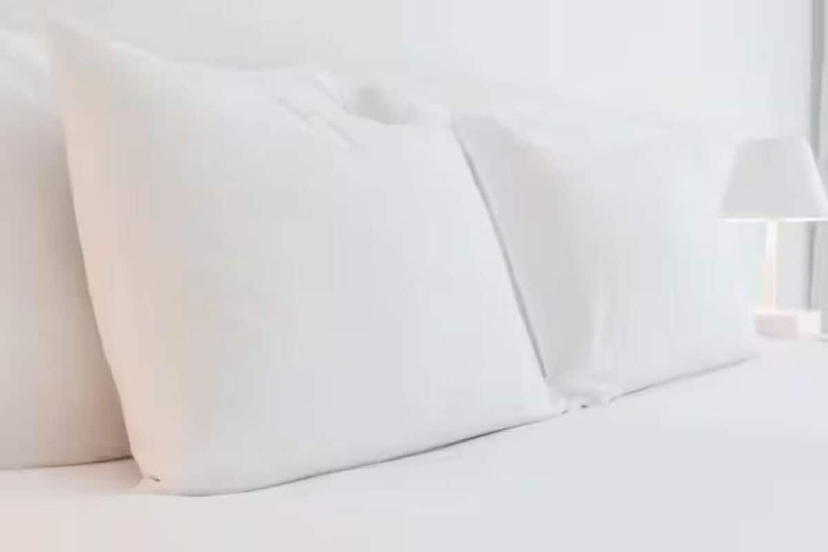 A neatly arranged bed with white bedding and pillows, a bedside lamp, and a white nightstand.