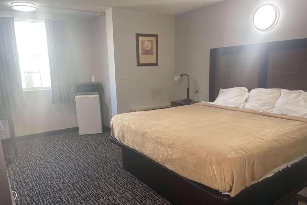 A hotel room with a bed, a desk, a chair, a lamp, a picture on the wall, and a window with curtains.