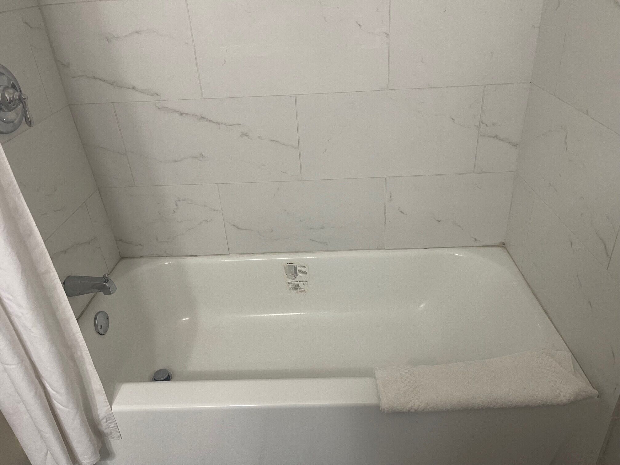 Un baño con una bañera blanca, una cortina de ducha y paredes con diseño de mármol.