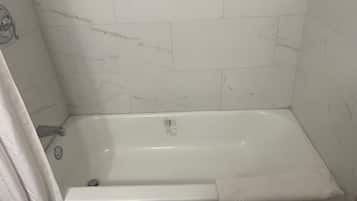Un baño con una bañera blanca, una cortina de ducha y paredes con diseño de mármol.
