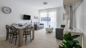 A modern living room with a dining area, a sofa, a TV, and a staircase. - Residence Medusa - 6 (Lido di Jesolo)