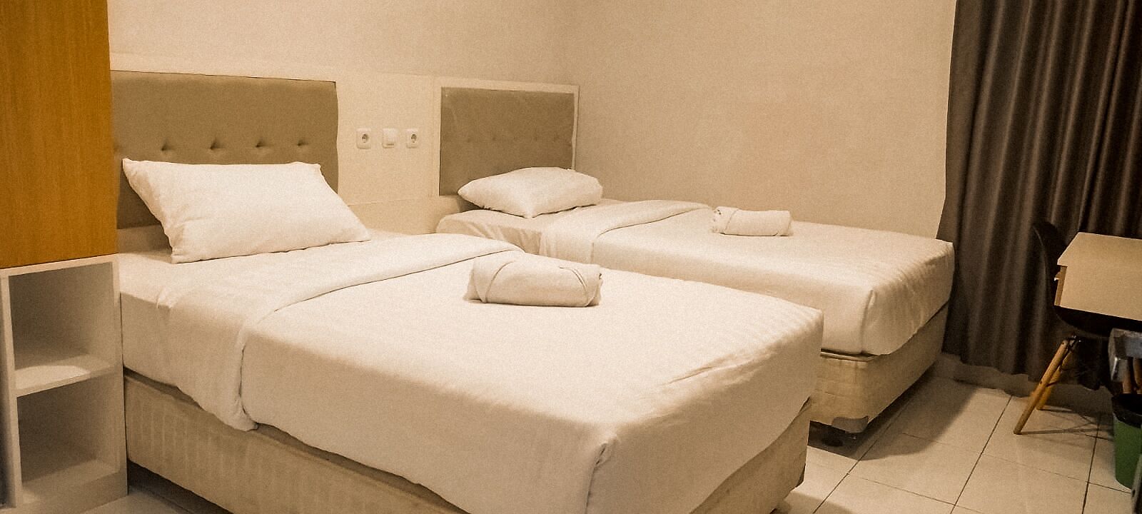 A hotel room with two beds, each with a headboard and pillows. There is a nightstand with a lamp and a box on the floor.