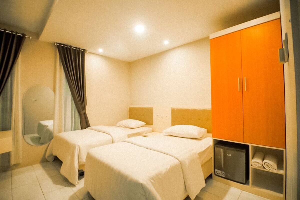 Quarto de hotel com duas camas de solteiro, um guarda-roupa, um espelho e um pequeno armário com toalhas.