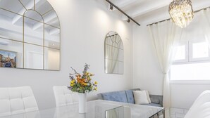 Un salon moderne avec une table à manger en verre, des canapés blancs, un canapé bleu, un grand miroir et un lustre.