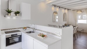 Une cuisine moderne dotée d’un îlot central, d’un four encastré et d’un coin repas agrémenté d’un lustre.