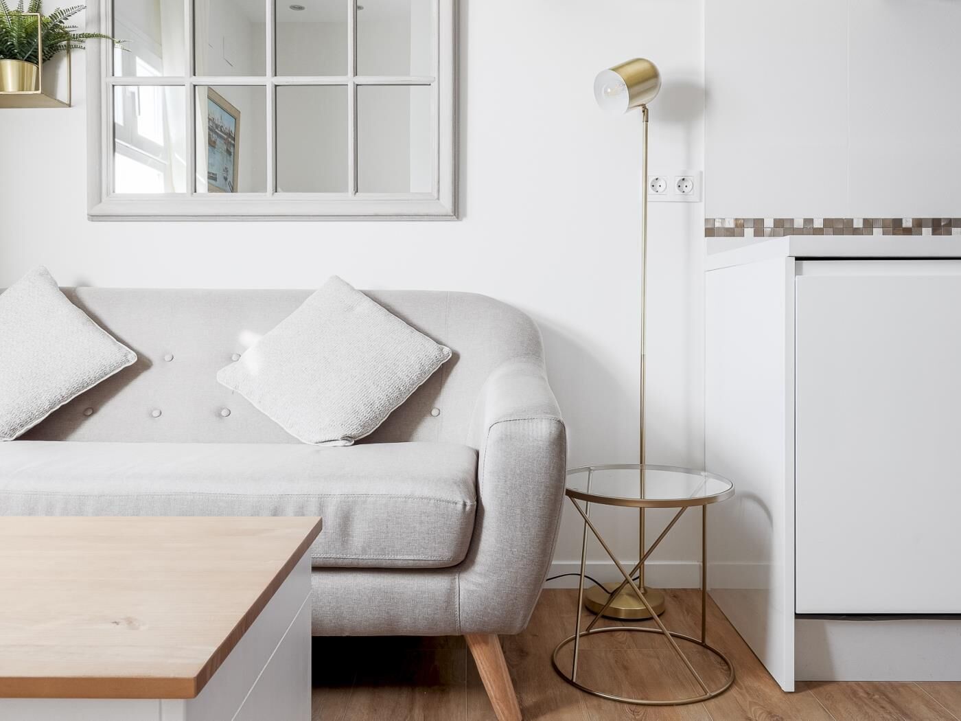 Ein modernes Wohnzimmer mit einem grauen Sofa, zwei weißen Kissen, einem Holztisch, einer Stehlampe und einer weißen Kommode mit Fliesenrückwand.