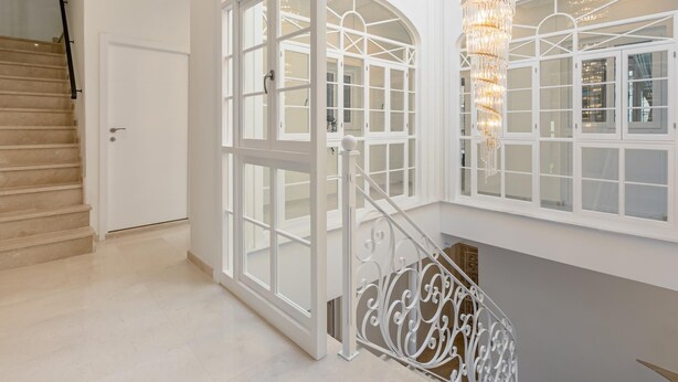 Ein großzügiger Innenraum mit einer imposanten Treppe, großen Rundbogenfenstern und einem dekorativen Kronleuchter.